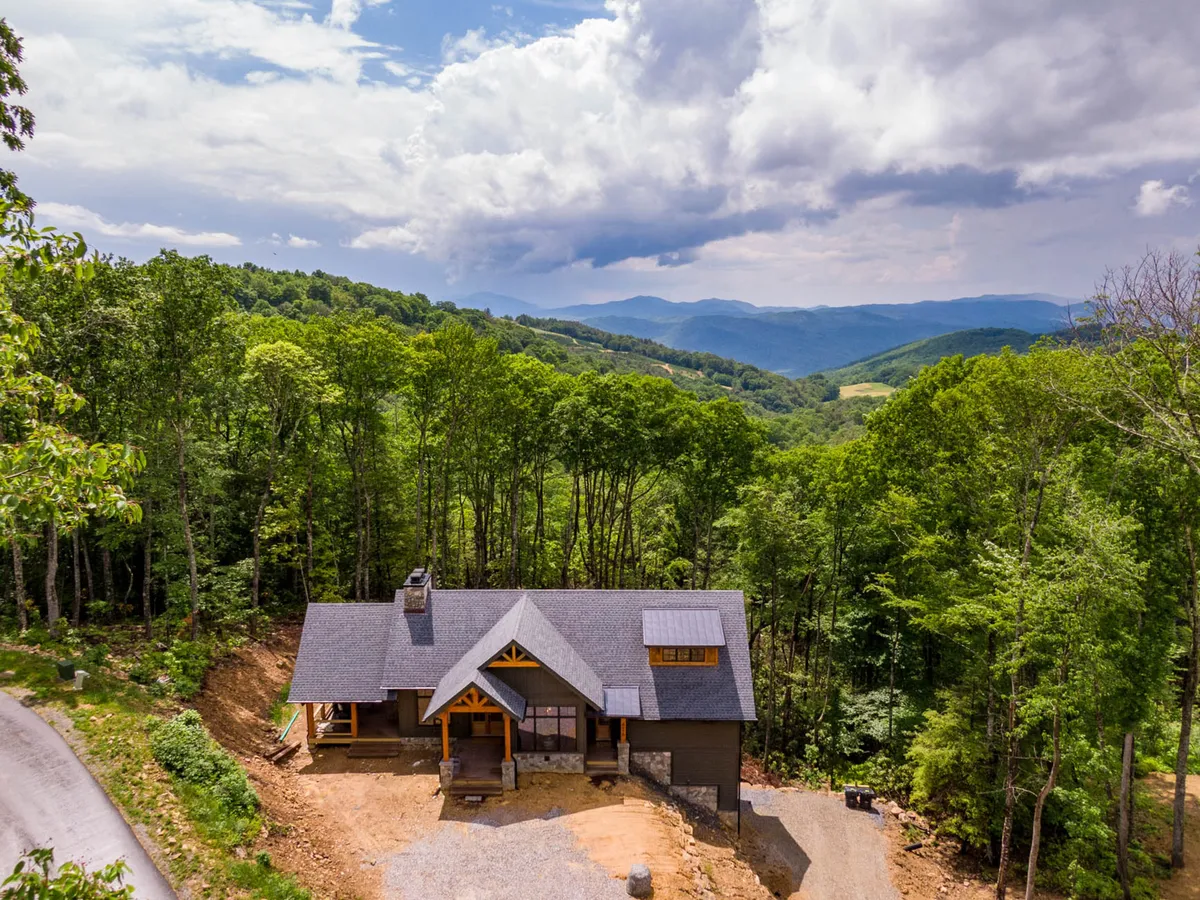 The home's architectural features are showcased amidst a backdrop of mountain views and lush trees. The exterior setting is tranquil, inviting guests to imagine hiking, nature walks, or simply relaxing outdoors.