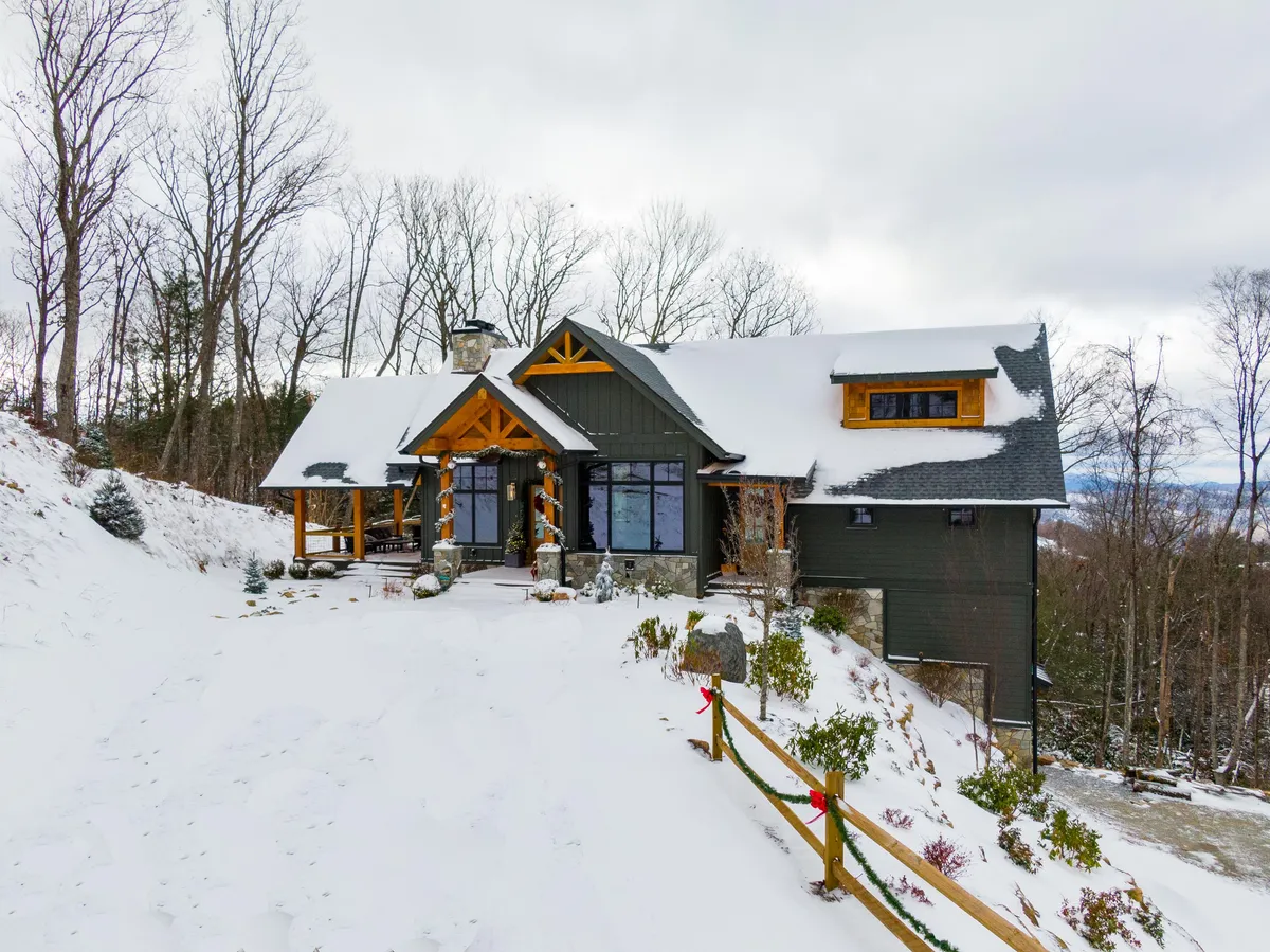 The entrance to the lodge, accented by decorative wooden beams and large windows that showcase glimpses of the inviting interior. The landscape is blanketed in snow, hinting at year-round outdoor fun and access to nearby trails.