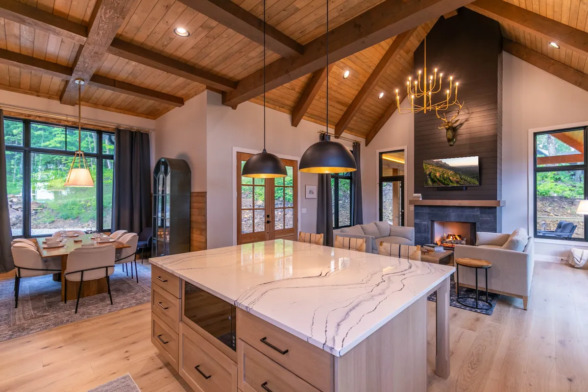 A harmonious open-plan living, dining, and kitchen space with a prominent kitchen island, inviting fireplace, dining table, and expansive windows overlooking the outdoors. The setup encourages conversation, relaxation, and shared meals in a unified space.
