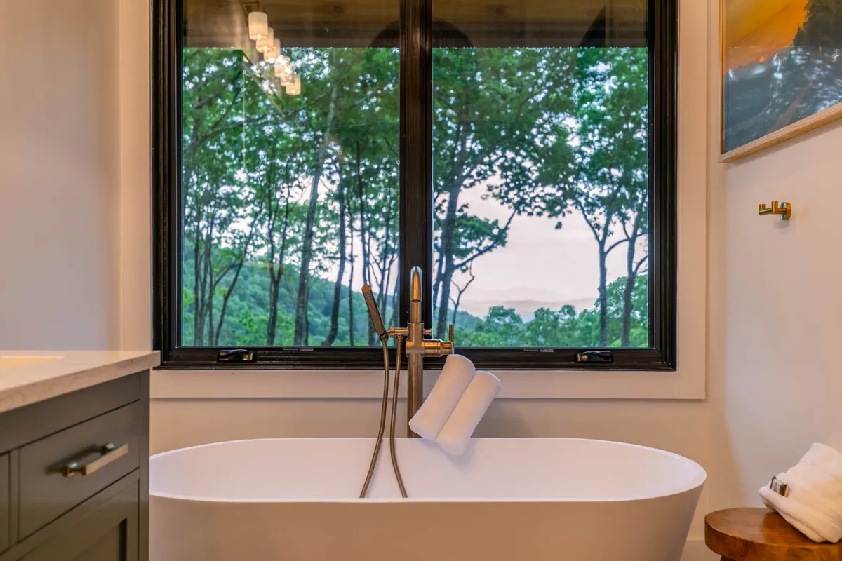 A freestanding soaking tub is set next to a large window, offering immersive views of the natural landscape outside. The bathroom exudes luxury and relaxation, perfect for unwinding after a day of adventure.
