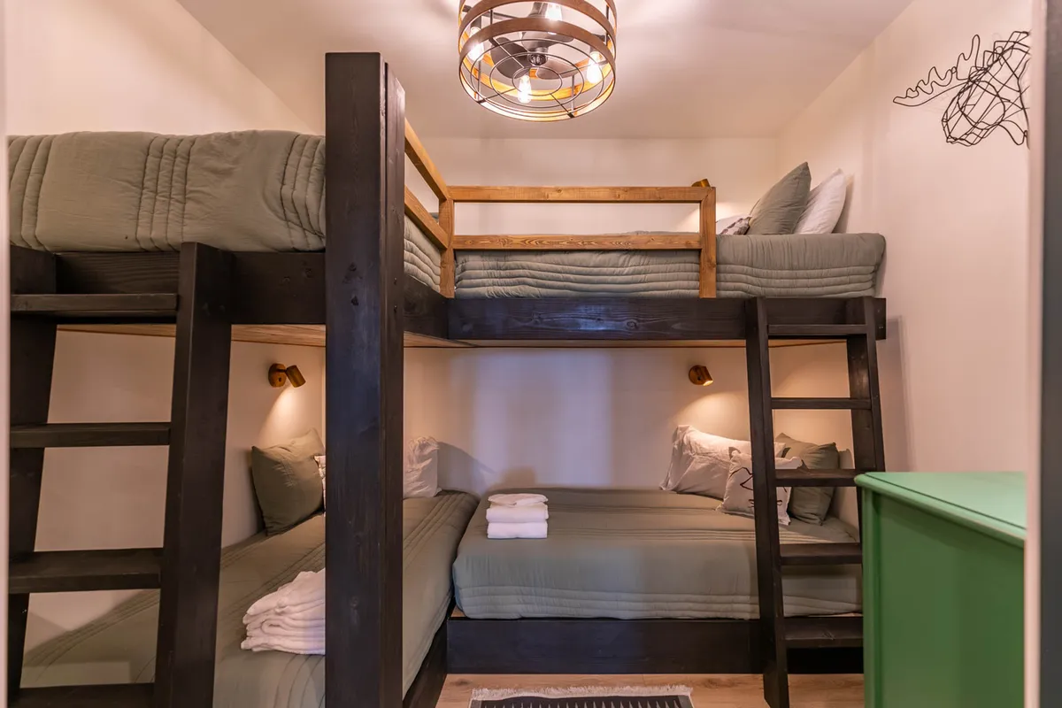 A cheerful bunk room with sturdy bunk beds, a playful green dresser, decorative wall art, and a whimsical light fixture. The space is designed for comfort and fun, making it perfect for kids or groups of friends.