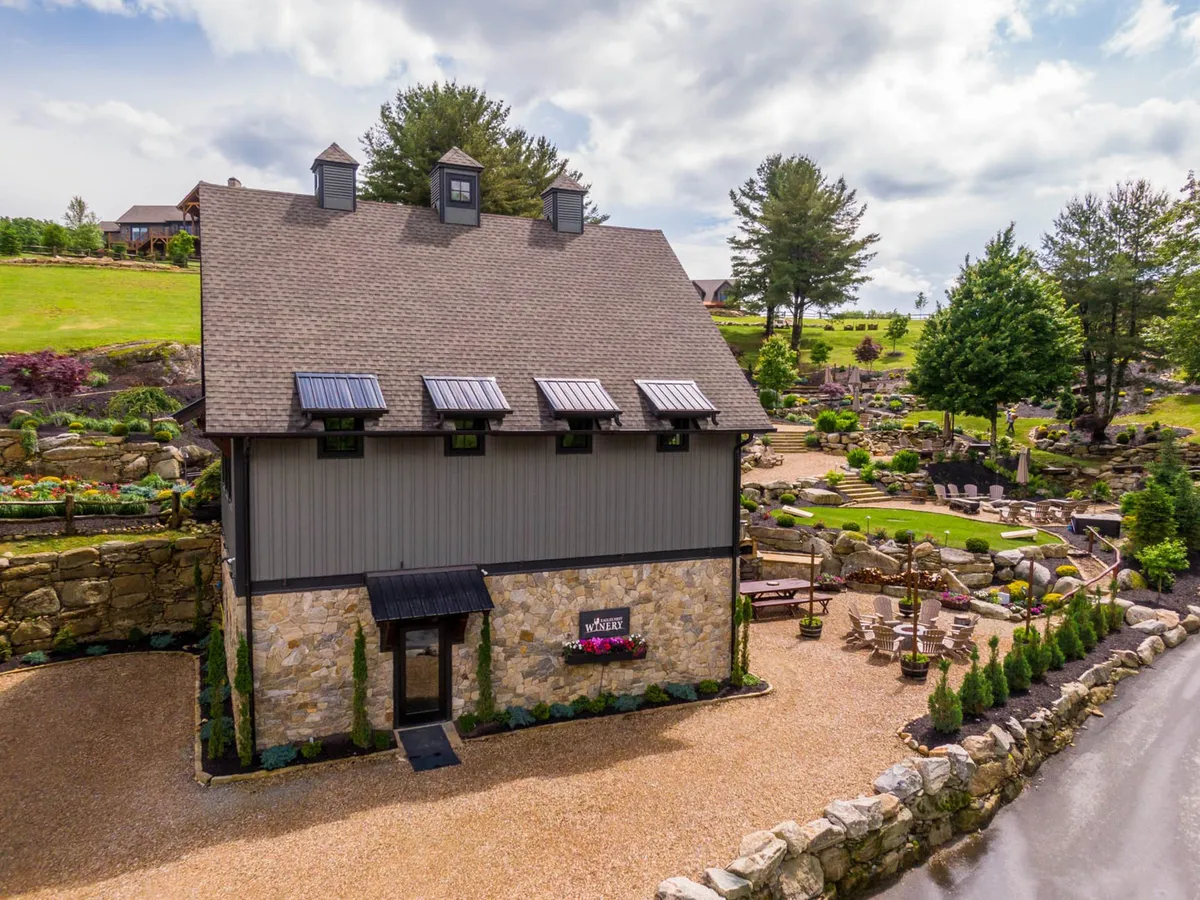 The image highlights a stone building facade with a landscaped garden and an inviting outdoor seating area. The setting suggests a tranquil atmosphere, ideal for gatherings, tastings, and social events under the open sky—paralleling the winery's inviting spaces.