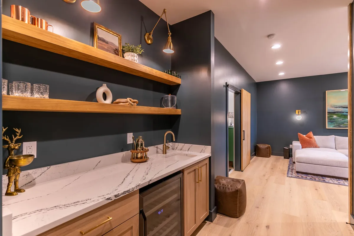 This image displays a marble countertop bar area with wooden shelves, contemporary artwork, a sofa, and an integrated bar space—ideal for preparing refreshments and encouraging social interaction.