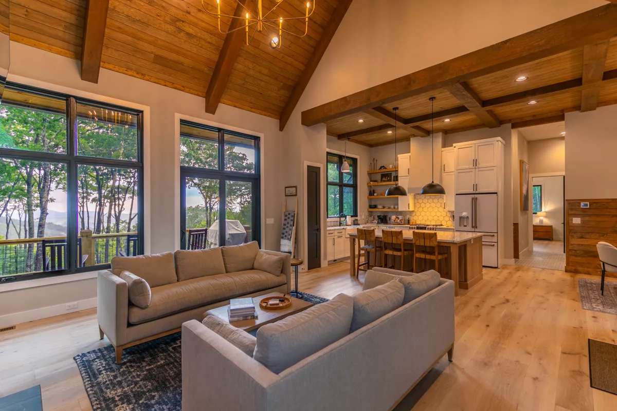 A cozy living space with a central kitchen island, comfortable sofas, large windows framing scenic outdoor views, and sophisticated chandelier lighting. The area feels welcoming and encourages shared experiences, from cooking to relaxing and enjoying sunsets.