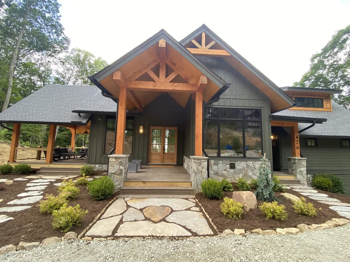 The hero image features the inviting exterior of the HeartStone Lodge, showcasing its impressive double-door entrance, grand wooden beams, and a charming stone pathway leading up to the porch. The warm glow of sunset bathes the house, emphasizing the cozy, welcoming ambiance and the natural beauty of the surrounding mountain landscape.