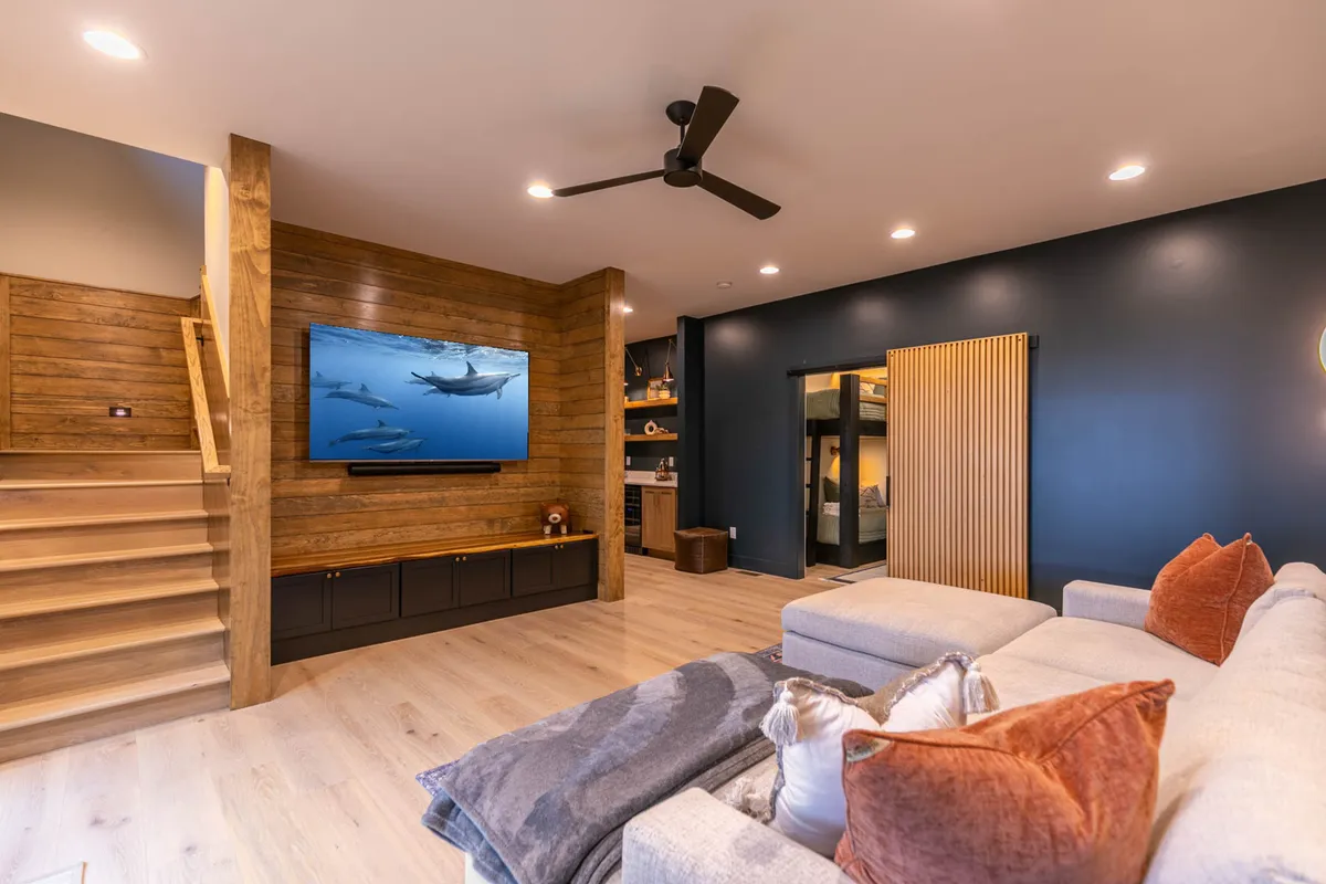 This image features a spacious den/media space with a large television displaying a vibrant marine scene, a comfortable sectional sofa with decorative cushions, and a textured wood panel wall. The overall ambiance is inviting and relaxed, perfect for movie nights and casual gatherings.